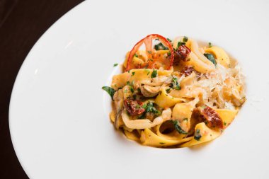 Beyaz tabakta tavuklu ve domatesli lezzetli makarna, siyah arka plan.