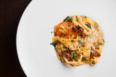 Beyaz tabakta tavuklu ve domatesli lezzetli makarna, siyah arka plan.