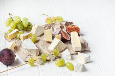Brie peyniri ve camembert peyniri beyaz ahşap bir masa üzerinde, üzümlü ve incirli.