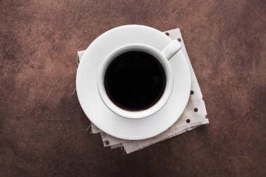 Peçetede beyaz kahve fincanı, klasik beton masa arka planı, üst manzara.