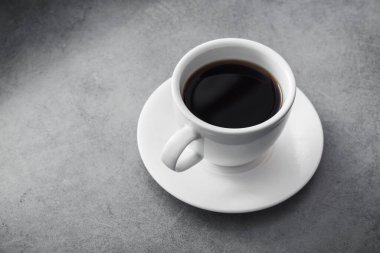 Beyaz seramik bardakta, taş masanın üzerinde siyah kahve.