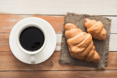 Ahşap bir masada tatlı kruvasanla bir fincan aroma kahvesi, Avrupa kahvaltısı, üst manzara.