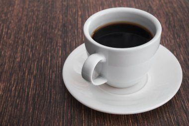 Beyaz kahve fincanı, ahşap masada siyah içecek.