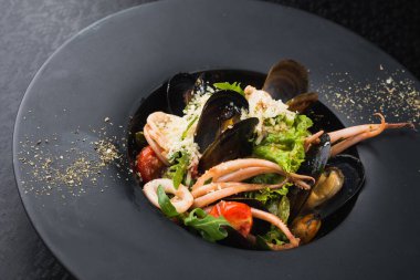 Siyah tabakta deniz ürünleri, mürekkep balığı ve midye. Restoranda yemek.