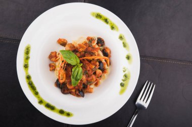 Zeytinli İtalyan makarnası, beyaz tabakta domates ve fesleğen, siyah masa, üst manzara.