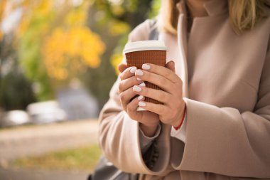 Kağıttan kahve fincanı taşıyan genç bir kadın. Parkta sonbahar yaşam tarzı kavramı.