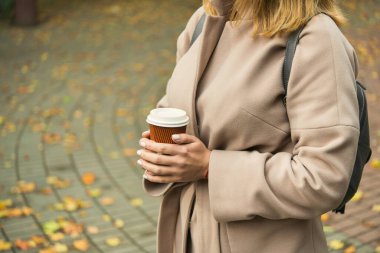 Kahve fincanı içen kadın, sonbahar havasında parkta yürüyen.