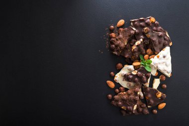 Siyah arka planda fındıklı siyah beyaz çikolata, taze nane ve badem.