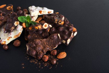Siyah arka planda fındıklı siyah beyaz çikolata, taze nane ve badem.