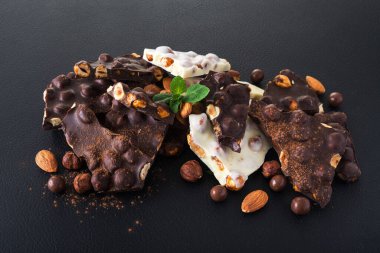 Siyah arka planda fındıklı siyah beyaz çikolata, taze nane ve badem.