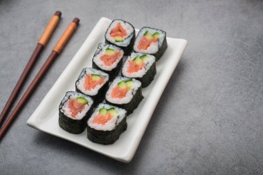 Somon ve salatalıklı suşi, yemek çubuğu taştan bir masada. Yukarıdan görünüm