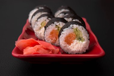 Somon balıklı suşi rulosu ve kırmızı tabakta Philadelphia. Siyah arka plan. Japon yemeği.