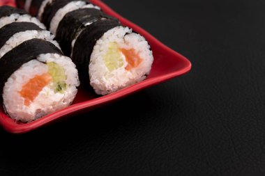 Somon balıklı suşi rulosu ve kırmızı tabakta Philadelphia. Siyah arka plan. Japon yemeği.
