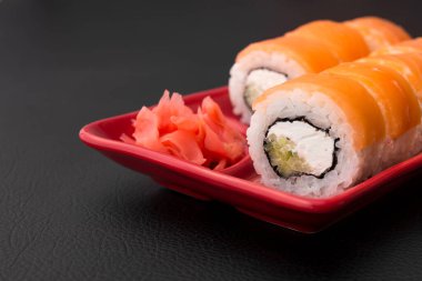 Somon balıklı suşi rulosu ve kırmızı tabakta Philadelphia. Siyah arka plan. Japon yemeği.