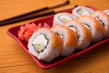 Somon balıklı suşi rulosu ve ahşap bambu masasında kırmızı masada Philadelphia. Lezzetli deniz ürünleri