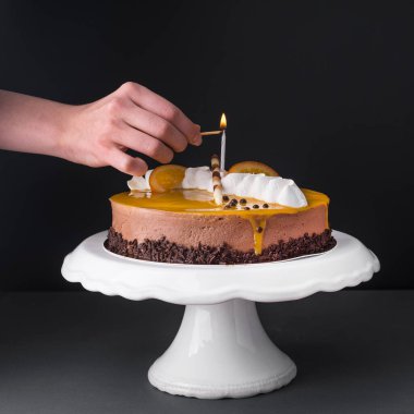 Siyah arka planda beyaz seramik standı üzerinde bir mum olan karamel kek.