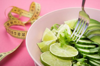 Avokado ile taze salata, yeşil limon ve pembe pastel arka planda salatalık. Diyet konsepti