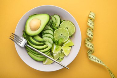 Avokado ile taze salata, yeşil limon ve pastel sarısı arkaplanda salatalık. Diyet konsepti yiyecekler. en üstteki görünüm