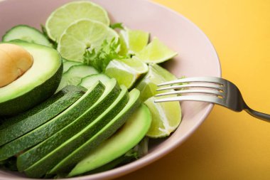 Avokado ile taze salata, yeşil limon ve pastel sarısı arkaplanda salatalık. Diyet konsepti