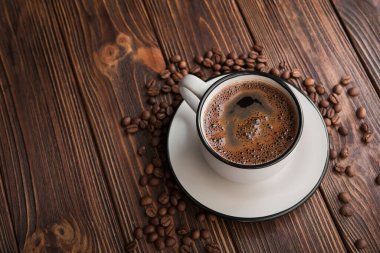 Ahşap bir masada kavrulmuş fasulyeli beyaz kahve fincanı. Aroma lezzetli köpük