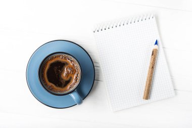 Not defteri ve kalemle kahve fincanı. Günün başlangıcı, davaların programı. Üst görünüm
