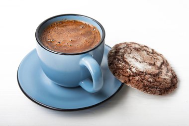 Beyaz ahşap masada çikolatalı kurabiye ile mavi kahve fincanı.