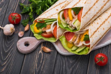 Tortilla, ahşap bir tahtanın üzerinde ızgara tavuk ve taze sebzelerle sarılır. Meksika fast food geçmişi. Üst görünüm.