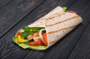 Tahta bir tahtanın üzerinde ızgara tavuk ve taze sebzeli bir tortilla dürümü. Meksika fast food geçmişi.