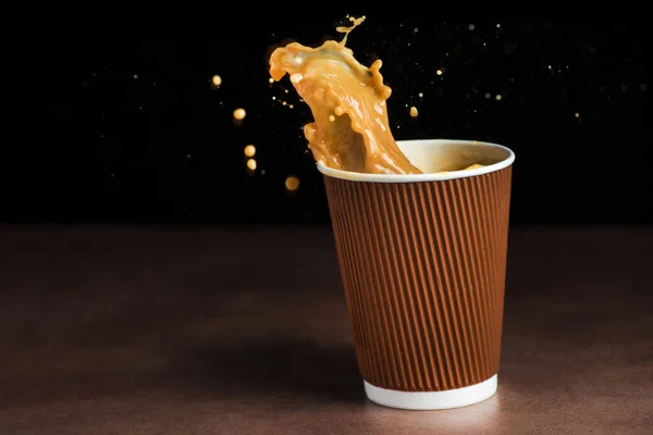 Splash of coffee in a paper takeaway cup on black background