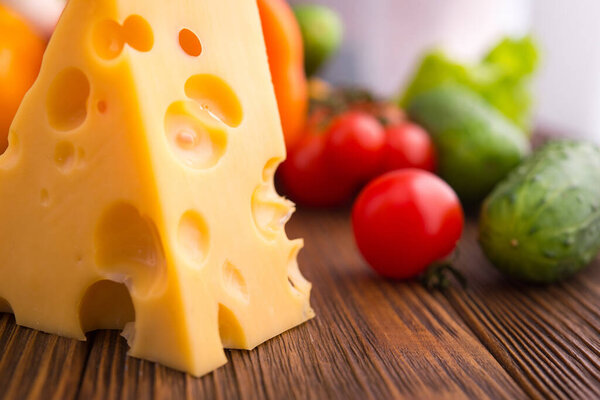 piece of cheese with fresh vegetables on a table. Dairy product background.