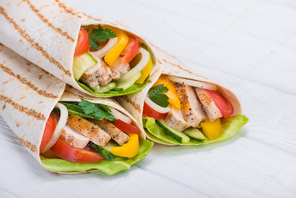 Tortilla wraps with grilled chicken and fresh vegetables on a wooden table. Mexican fast food background.