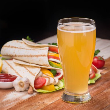 Kızarmış tavuk, taze sebze ve bir bardak birayla ahşap bir masaya sarılmış tortilla. Meksika fast food konsepti.