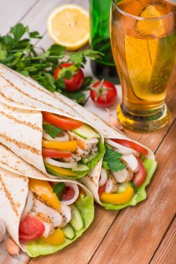 Kızarmış tavuk, taze sebze ve bir bardak birayla ahşap bir masaya sarılmış tortilla. Meksika fast food konsepti.