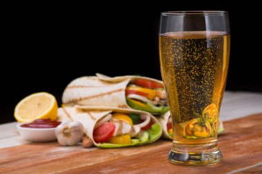 Kızarmış tavuk, taze sebze ve bir bardak birayla ahşap bir masaya sarılmış tortilla. Meksika fast food konsepti.