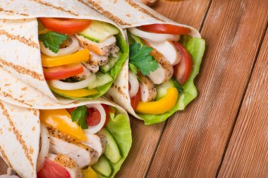 Tortilla ızgara tavuk ve taze sebzelerle ahşap bir masaya sarılır. Meksika fast food geçmişi. Üst görünüm.