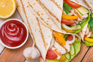 Tortilla ızgara tavuk ve taze sebzelerle ahşap bir masaya sarılır. Meksika fast food geçmişi. Üst görünüm.