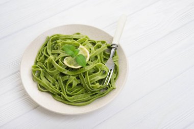 Beyaz ahşap masaya izole edilmiş fesleğenli yeşil ıspanaklı tagliatelle makarna.