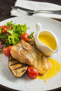 Sebzeli balık bifteği ve beyaz tabakta sos.