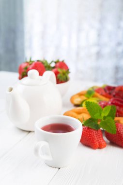 Meyve çayı ve çilekli tatlı fırın, şeker kaplı kivi, beyaz ahşap masa. Yaz tatlıları..