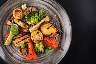 Tabakta ızgara sebze ve fesleğen yaprağı. Karanlık arka plan. en üstteki görünüm