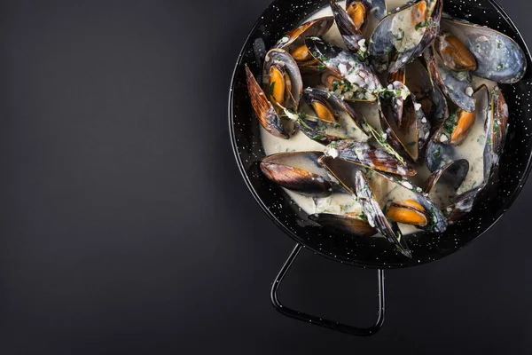 Shell mussels in a frying pan with chesse and sauce on a black background. top view