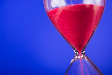 Mavi arka planda kum saati olan parlak pembe kum.