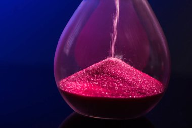 Mavi arka planda kum saati olan parlak pembe kum.