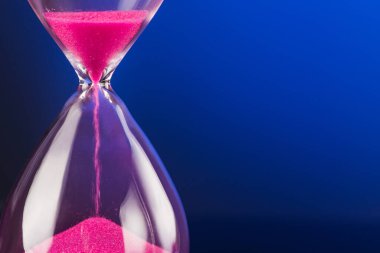 Mavi arka planda kum saati olan parlak pembe kum.