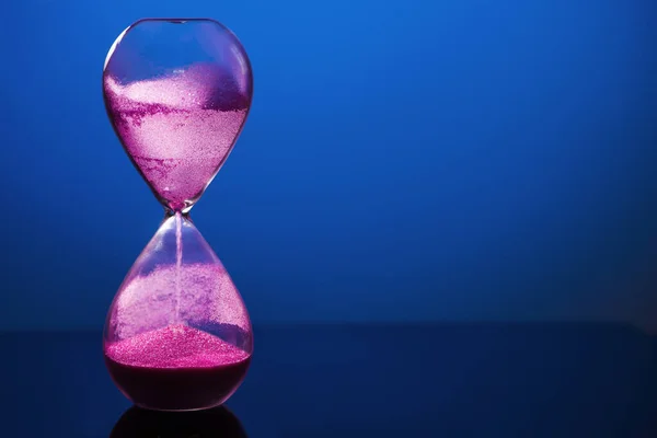 青の背景に砂時計と明るいピンクの砂 — ストック写真