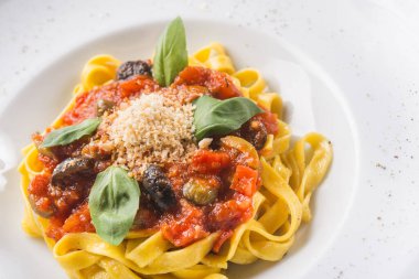 Beyaz tabakta domatesli, zeytinli ve fesleğenli İtalyan makarnası. popüler yemek