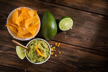 Guacamole soslu kase ve ahşap masada cips.