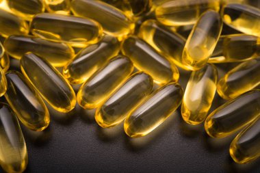 Siyah arka planda altın balık yağı kapsülü. Omega 3 hapları..