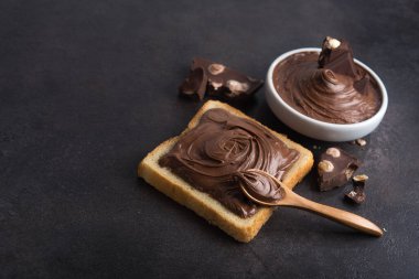 Çikolata, kaşıkla bir dilim ekmeğe, erimiş krema beyaz kâsesine ve taş bir masada fındıklı çikolataya sürüldü. Popüler tatlı yiyecekler.