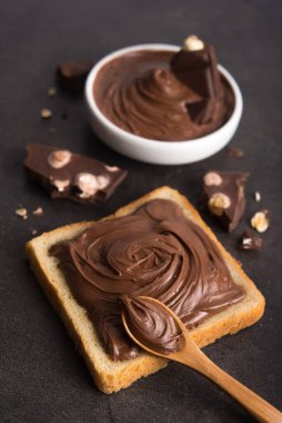 Çikolata, kaşıkla bir dilim ekmeğe, erimiş krema beyaz kâsesine ve taş bir masada fındıklı çikolataya sürüldü. Popüler tatlı yiyecekler.